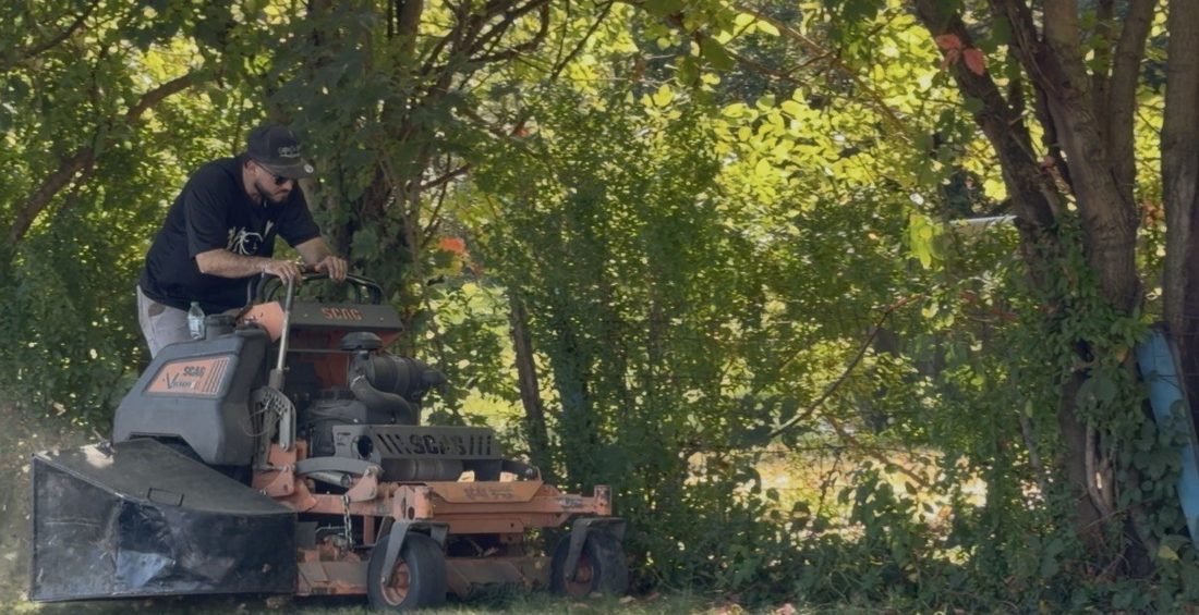 A V.O.V crew member mowing under a canopy of trees