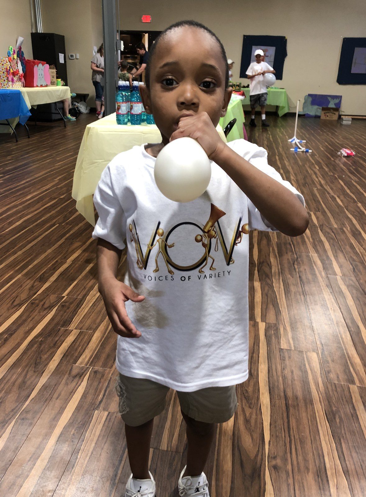 A young boy in a V.O.V shirt blowing up a balloon at a community event