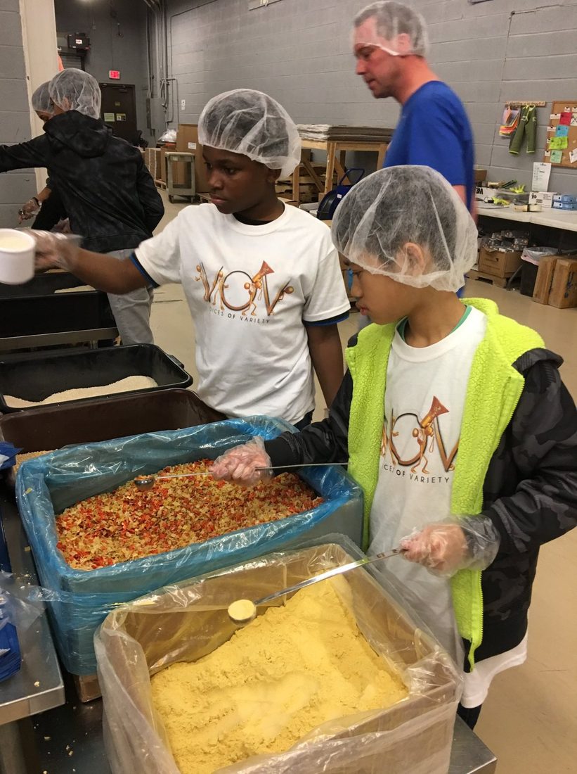 V.O.V youth in hairnets carefully measuring ingredients while packing meals