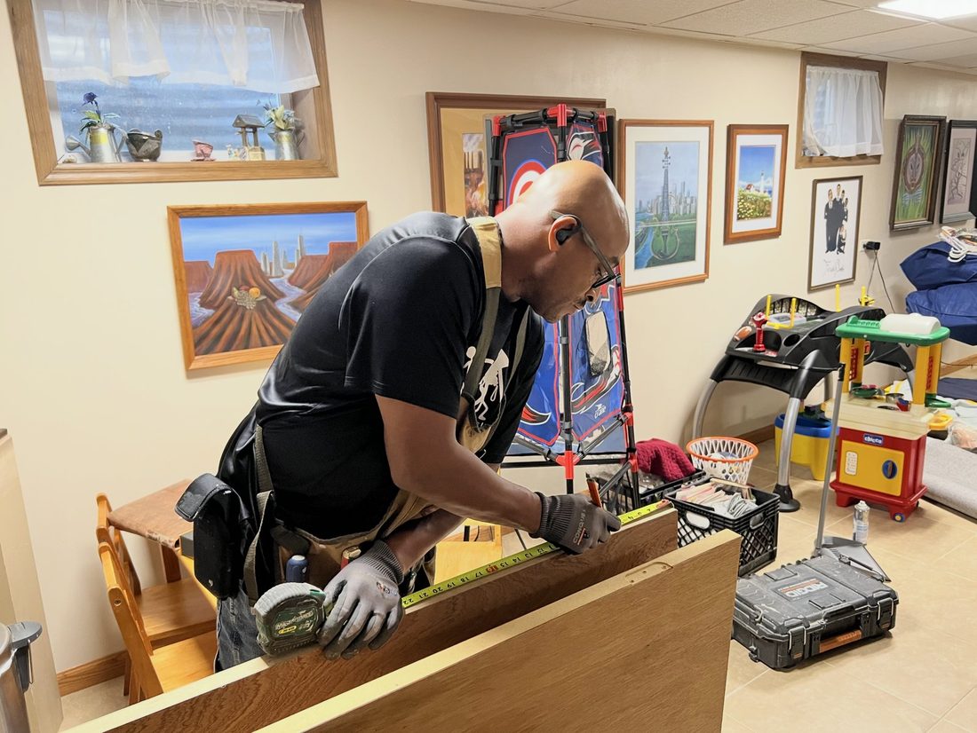 A V.O.V member measuring cabinet work in a rec room